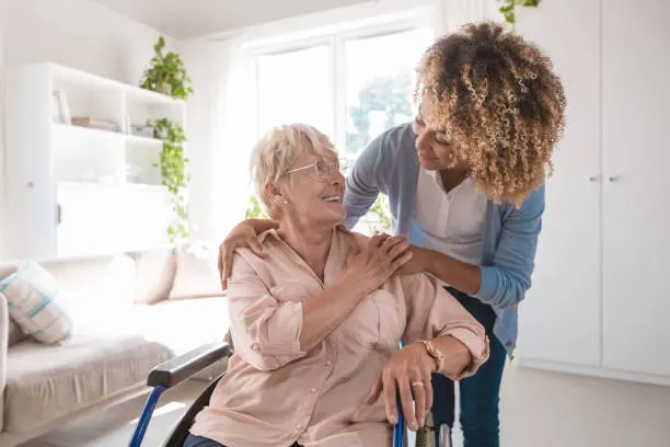 A caregiver embracing a smiling older woman in a wheelchair at home